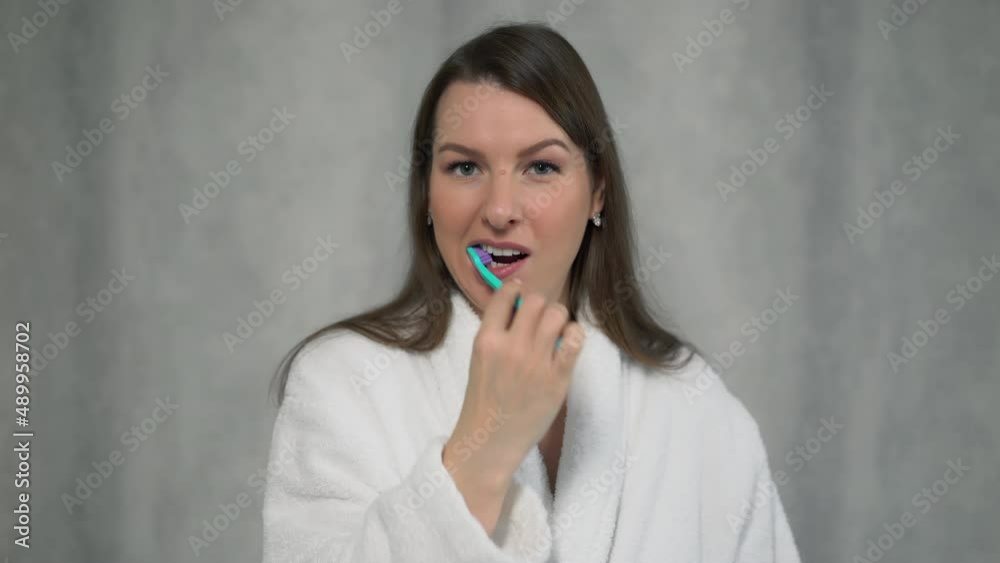 Woman in white bathrobe cleans her teeth with toothbrush and paste after shower. Woman in white bathrobe cleans her teeth with toothbrush and paste after shower.