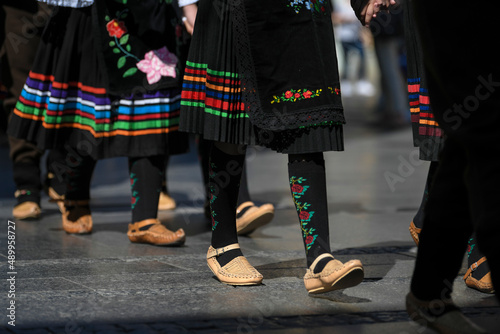 Closeup of opanci (peasant shoes) and traditional handmade folk costume from the Republic of Serbia on national parade or festival. People walking and dancing on street festival.