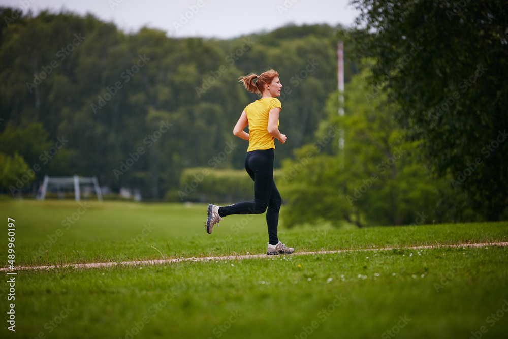 Taking in a park run. Shot of a woman jogging along a foothpath in a park.