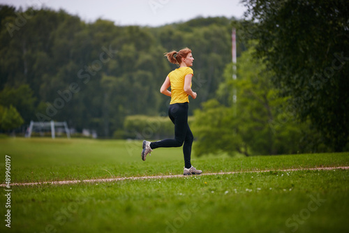 Taking in a park run. Shot of a woman jogging along a foothpath in a park.