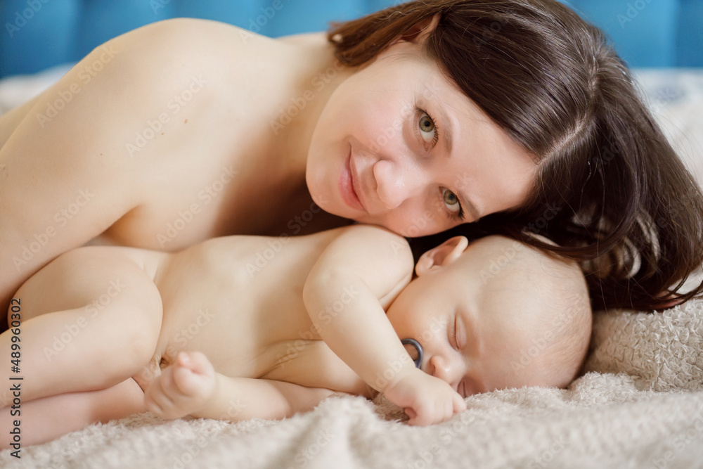 a beautiful naked baby sleeps near his mother on bed. happiness of motherhood. a beautiful naked baby sleeps near his mother on bed. happiness of motherhood.