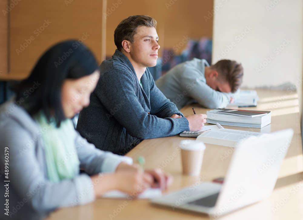 Cramming some last minute knowledge. A young man studying the library with other students. Cramming some last minute knowledge. A young man studying the library with other students.