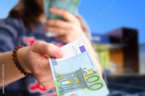 Female hand giving only one money banknote for a payment on bank background, close up of caucasian adult lady handing out European Union currency, euro. Selective focus on money.