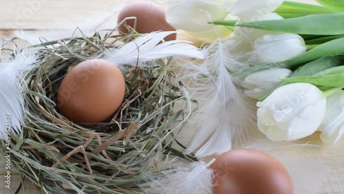 Basket easter decoration: natural colour eggs in basket with spring tulips, white feathers on wooden table background. Congratulatory easter design