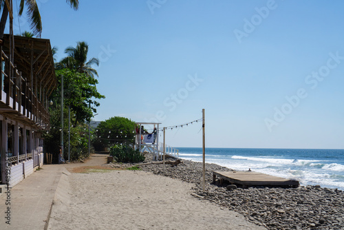 El Tunco, El Salvador - January 29, 2022: Rocky beach with buildings on a summer day. Lifeguards standing on the chair