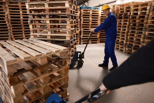 Workers moving wooden pallets with manual forklift in warehouse © New Africa