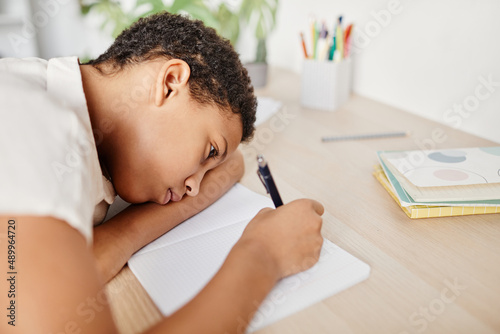 Carta da parati Portrait of sad and bored child laying head on desk while struggling with homewo