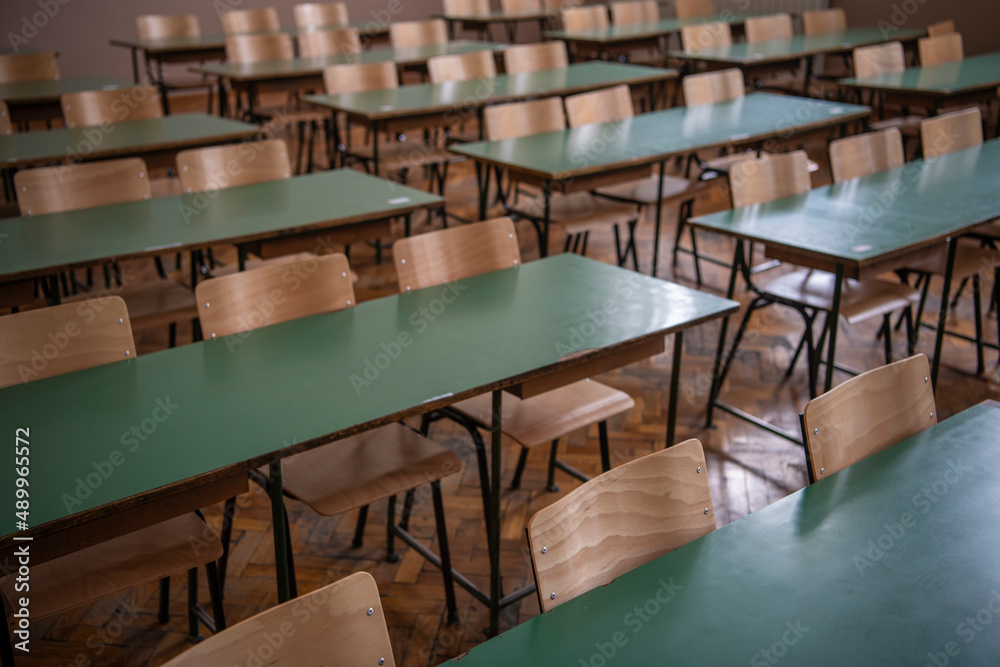 Empty old faculty or college School classroom with row of chairs and green desk tables. Natural light.