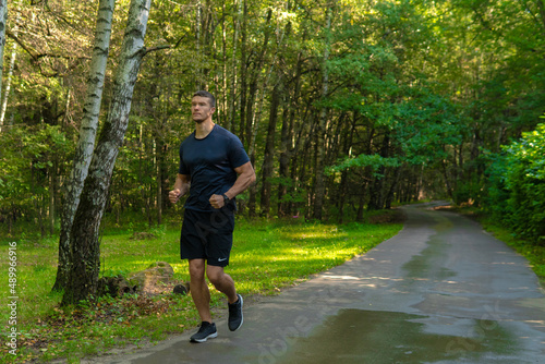 A man athlete runs in the park outdoors, around the forest, oak trees green grass young enduring athletic athlete run sport nature, fitness athletic legs woods outside. Summer cross, runners stretches