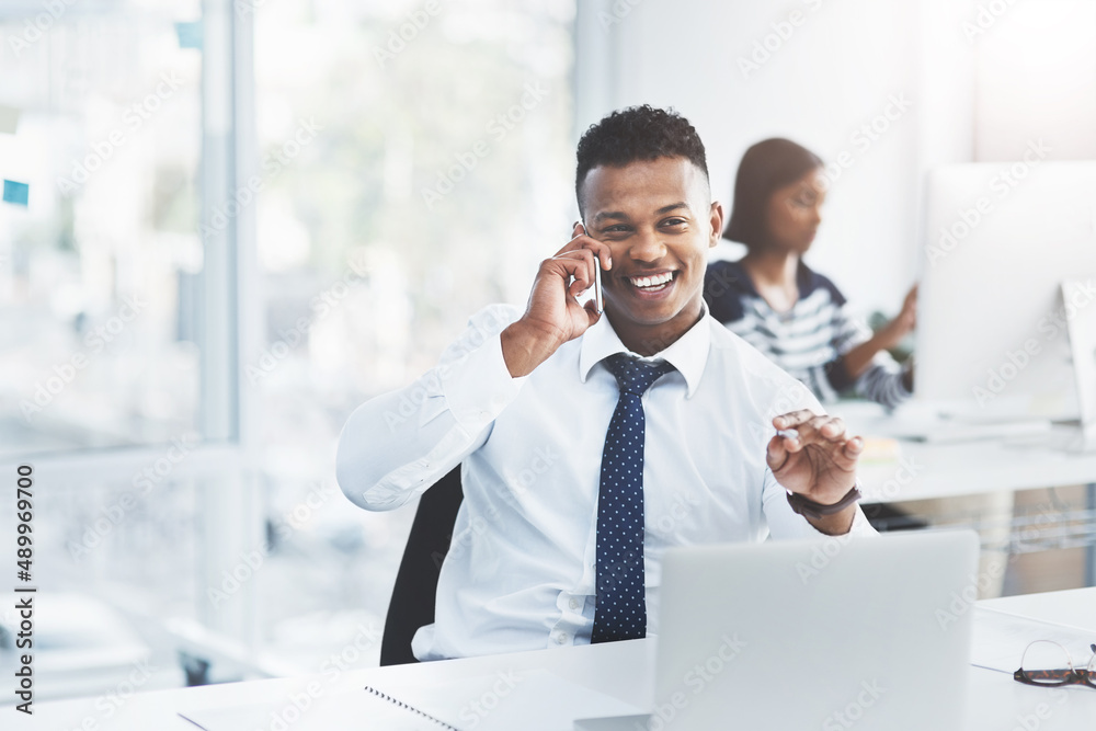 Things always go according to plan when youve planned ahead. Shot of a young businessman making a phone call at his office desk with a colleague working in the background. Things always go according to plan when youve planned ahead. Shot of a young businessman making a phone call at his office desk with a colleague working in the background.