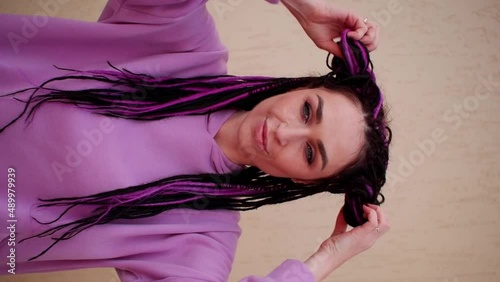 A young girl undoes her hair from colored braids and combs her pigtails with her fingers.