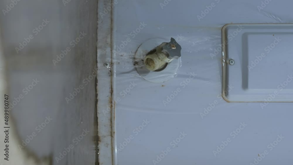 A vertical closeup shot of an electric water heater leaking from the