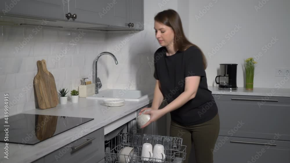 Young woman in the kitchen opens the dishwasher, loads and takes out dishes. Young woman in the kitchen opens the dishwasher, loads and takes out dishes.