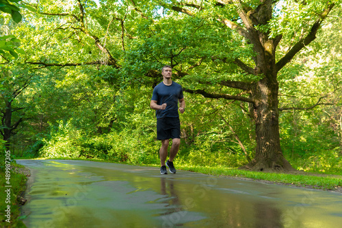 A man athlete runs in the park outdoors, around the forest, oak trees green grass young enduring athletic athlete run sport forest, lifestyle athletic jog, jogging outside. Autumn leisure running