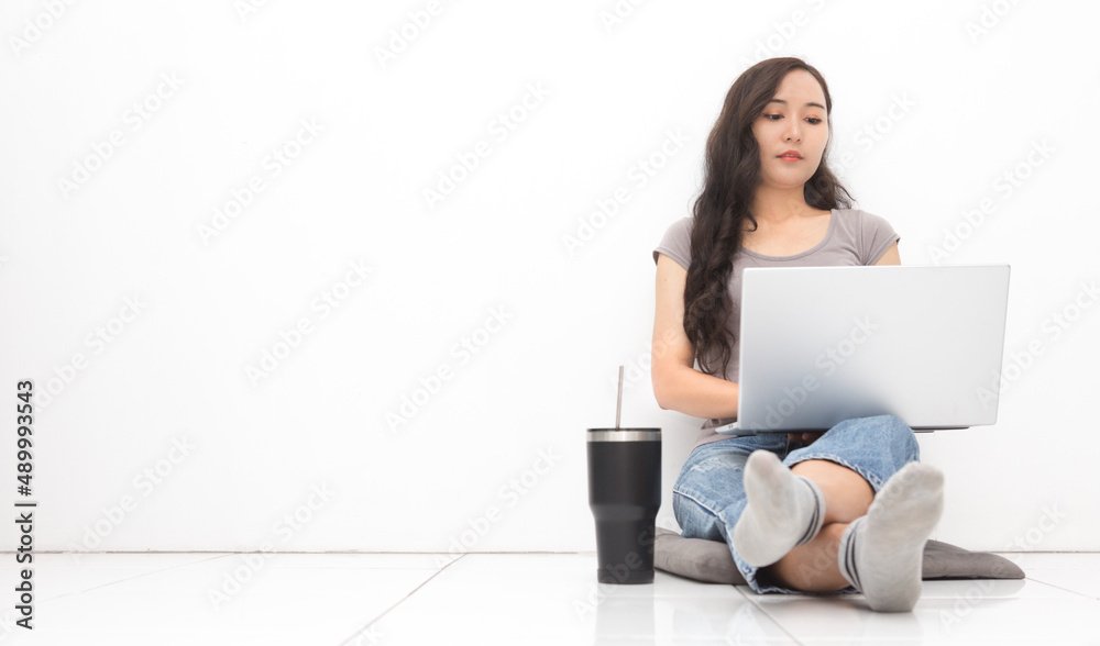 Beautiful Asian woman wearing grey casual shirt using laptop on white background and copy space. Cute Asian woman sitting on the floor room relaxing for work from home concept Beautiful Asian woman wearing grey casual shirt using laptop on white background and copy space. Cute Asian woman sitting on the floor room relaxing for work from home concept