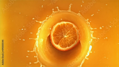 A round piece of fresh orange falls into orange juice with splashes. Top view. Macro background.Filmed is slow motion 1000 fps.
