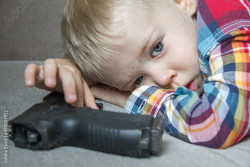 Sad kid with a gun. Child and weapons, unsafety storage, suicide photo