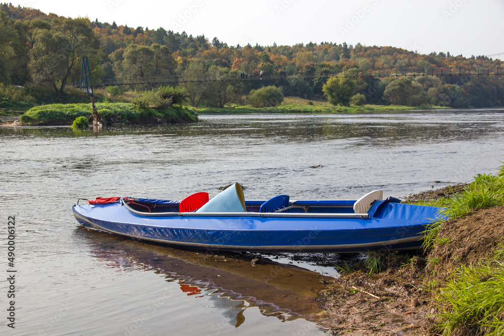 Fototapeta premium Kayak on the river bank. Blue canoe and scenic lake before the trip.