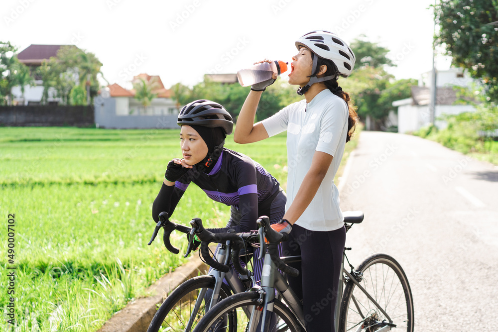 female cyclist having a bottle of water on the road side