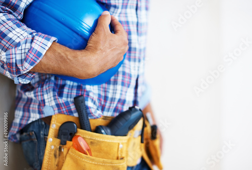 Construction worker holding protective helmet. Mid section of construction worker with tool belt holding blue protective helmet. © Stigur/peopleimages.com