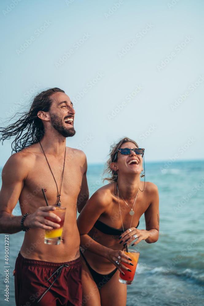 Fototapeta premium Attractive young couple with alcohol cocktails walking on the beach