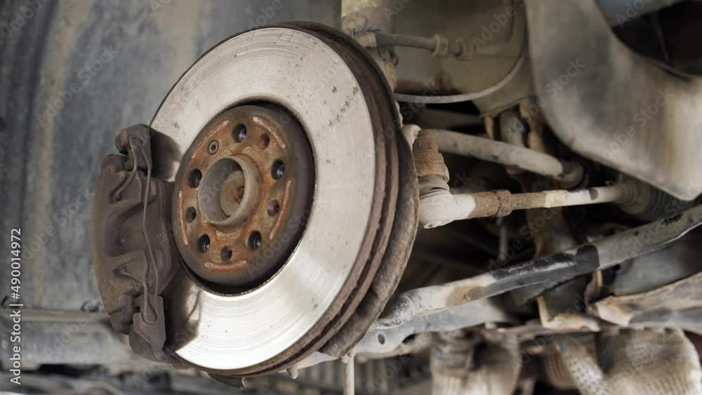 hands of the master with a key open the nut of the front suspension of the car. brake disc, caliper, tie rod, lever