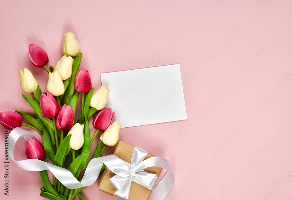 Bouquet of tulips, a gift box and a paper card on a pink background. Top view with place for text. Greeting on the occasion of Women's or Mother's Day. Bouquet of tulips, a gift box and a paper card on a pink background. Top view with place for text. Greeting on the occasion of Women's or Mother's Day.