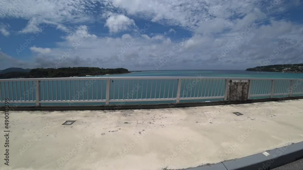 OKINAWA, JAPAN - AUG 2021 : Driving around Kouri Island bridge in sunny summer day. Wide camera, point of view (POV), seaside road driving. Holiday, vacation and resort concept. OKINAWA, JAPAN - AUG 2021 : Driving around Kouri Island bridge in sunny summer day. Wide camera, point of view (POV), seaside road driving. Holiday, vacation and resort concept.