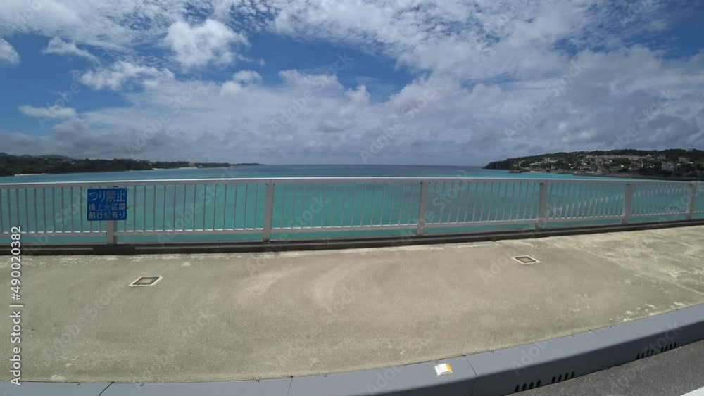OKINAWA, JAPAN - AUG 2021 : Driving around Kouri Island bridge in sunny summer day. Wide camera, point of view (POV), seaside road driving. Holiday, vacation and resort concept. OKINAWA, JAPAN - AUG 2021 : Driving around Kouri Island bridge in sunny summer day. Wide camera, point of view (POV), seaside road driving. Holiday, vacation and resort concept.