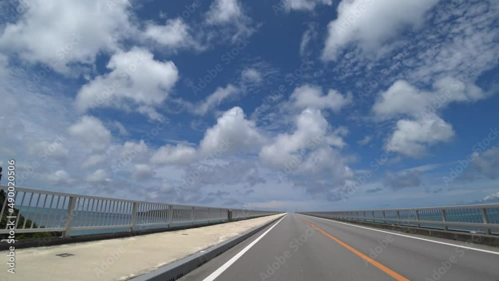 OKINAWA, JAPAN - AUG 2021 : Driving around Kouri Island bridge in sunny summer day. Wide camera, point of view (POV), seaside road driving. Holiday, vacation and resort concept. OKINAWA, JAPAN - AUG 2021 : Driving around Kouri Island bridge in sunny summer day. Wide camera, point of view (POV), seaside road driving. Holiday, vacation and resort concept.