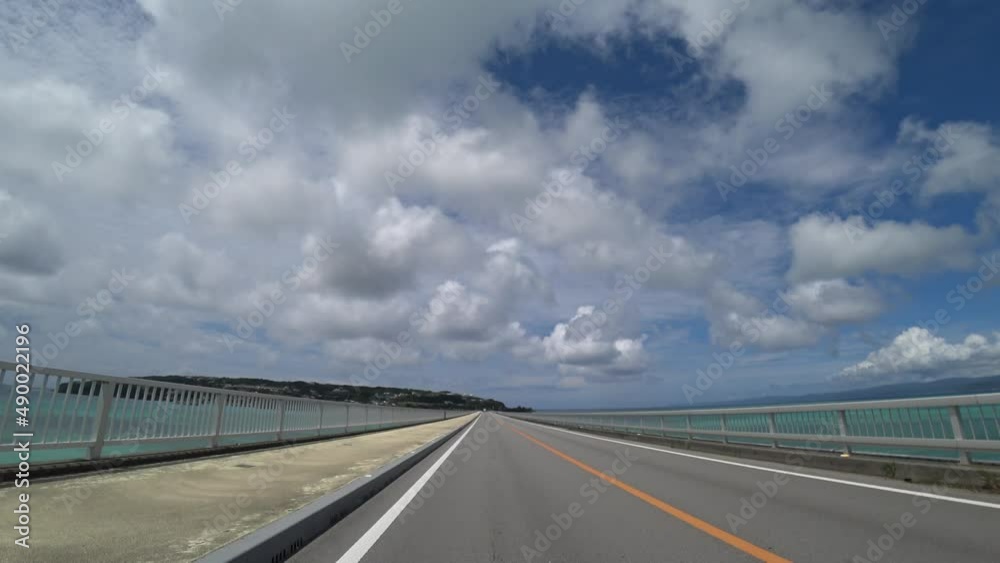 OKINAWA, JAPAN - AUG 2021 : Driving around Kouri Island bridge in sunny summer day. Wide camera, point of view (POV), seaside road driving. Holiday, vacation and resort concept. OKINAWA, JAPAN - AUG 2021 : Driving around Kouri Island bridge in sunny summer day. Wide camera, point of view (POV), seaside road driving. Holiday, vacation and resort concept.