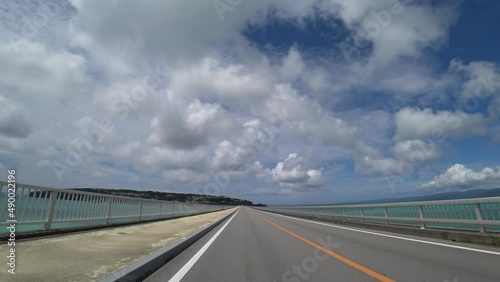 OKINAWA, JAPAN - AUG 2021 : Driving around Kouri Island bridge in sunny summer day. Wide camera, point of view (POV), seaside road driving. Holiday, vacation and resort concept. photo