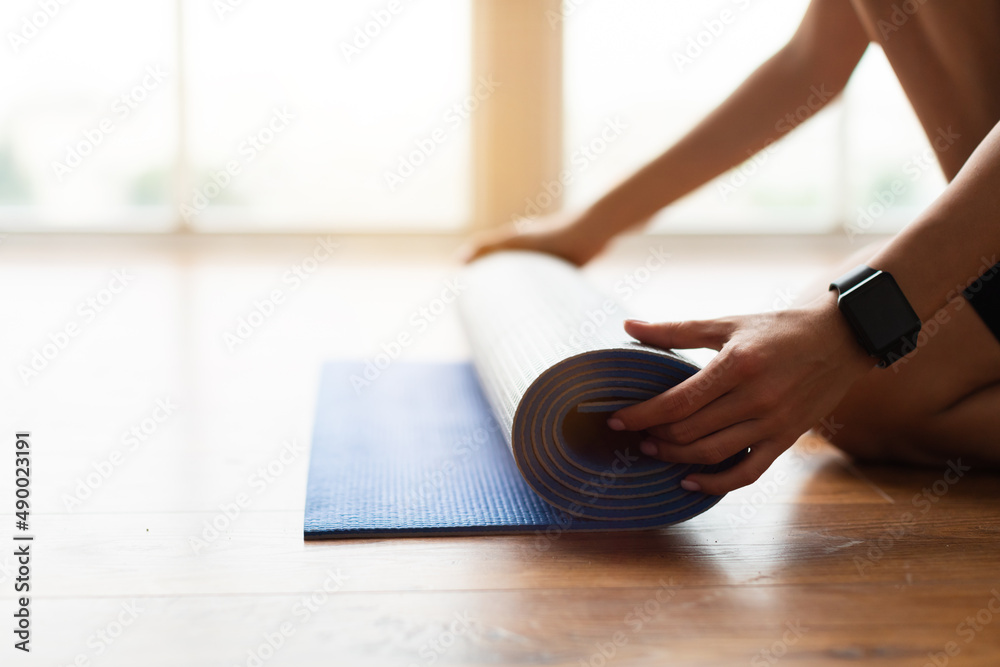 Fototapeta premium Closeup of young woman unrolling yoga mat on floor