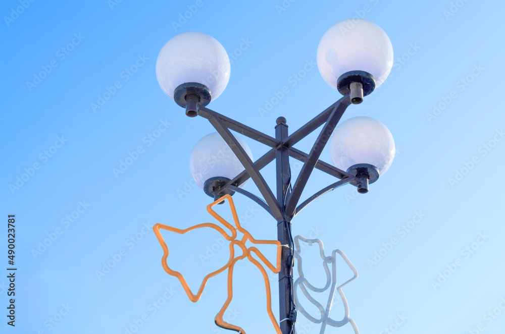 Street lamp on a blue sky background. Ornaments are hung on a lamppost. Street lamp on a blue sky background. Ornaments are hung on a lamppost.