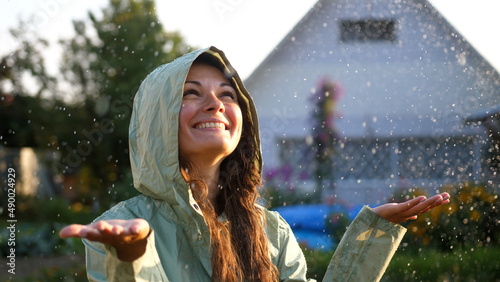 Young happy woman wearing green raincoat is feeling free and smiling under the rain. Concept of life, freedom, nature, adventure, purity.