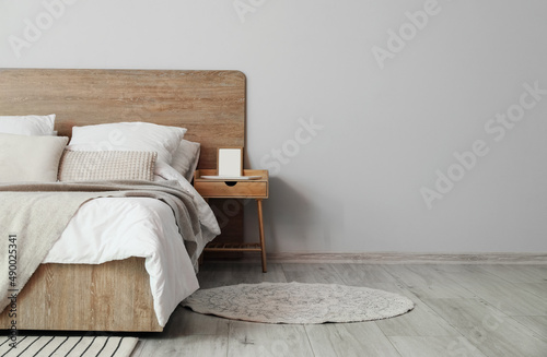 Fototapeta Naklejka Na Ścianę i Meble -  Comfortable bed and nightstand with blank frame near light wall