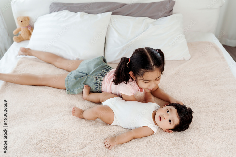 The happiness of two Asian brothers. The sisters are taking care of the 2-month-old newborn in bed in the bedroom with love and warmth. Concept Happy Family The happiness of two Asian brothers. The sisters are taking care of the 2-month-old newborn in bed in the bedroom with love and warmth. Concept Happy Family