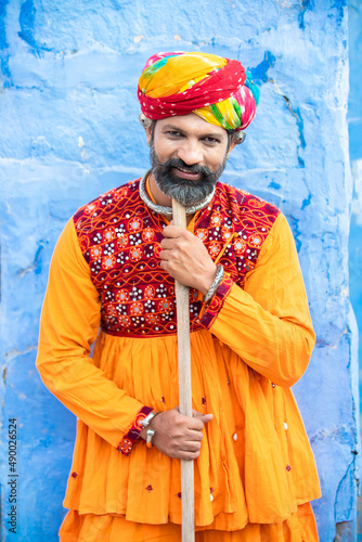 Fototapeta Happy traditional north indian man wearing colorful attire holding wood stick