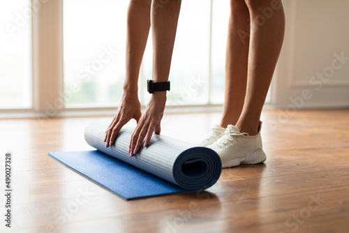 Closeup of young woman unrolling yoga mat on floor