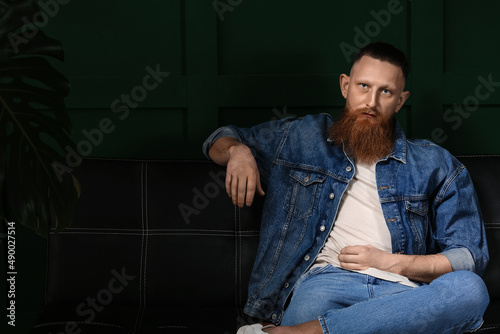 Portrait of handsome bearded man sitting on sofa in dark room
