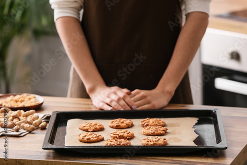 Fotografi Woman with baking sheet of tasty peanut cookies at kitchen table, closeup