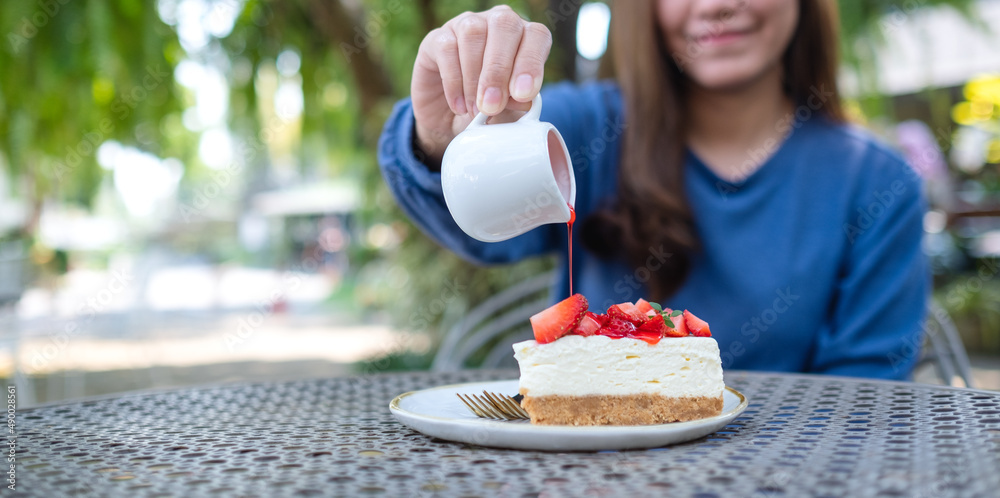 Blurred closeup image of a young woman pouring sauce onto a piece of strawberry cheese cake