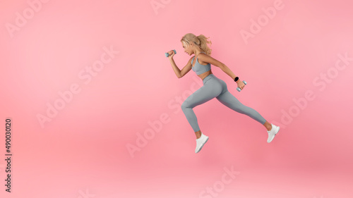 Young Woman Running With Dumbbells Isolated On Studio Background