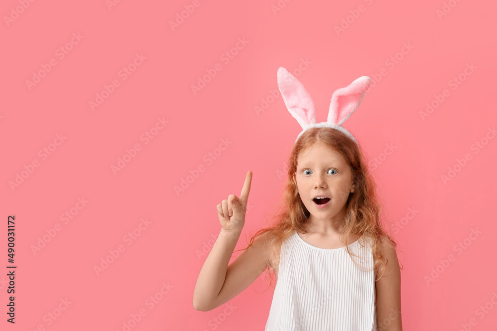 Funny redhead girl with bunny ears and raised index finger on color background. Easter celebration Funny redhead girl with bunny ears and raised index finger on color background. Easter celebration