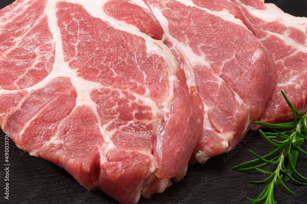 sliced raw pork meat with rosemar on black round stone plate isolated on white background. Clipping path and full depth of field sliced raw pork meat with rosemar on black round stone plate isolated on white background. Clipping path and full depth of field