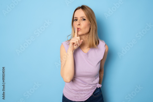 Young woman in casual t-shirt making silence gesture standing isolated over blue background.