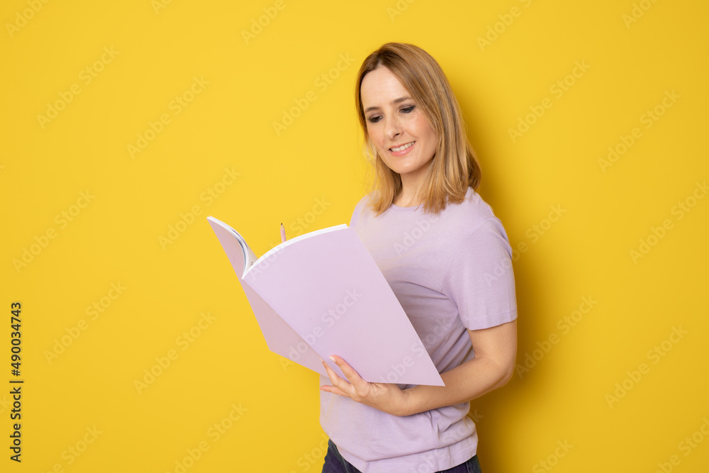 Young smiling woman making notes in a notebook smiling against a yellow background. Young smiling woman making notes in a notebook smiling against a yellow background.