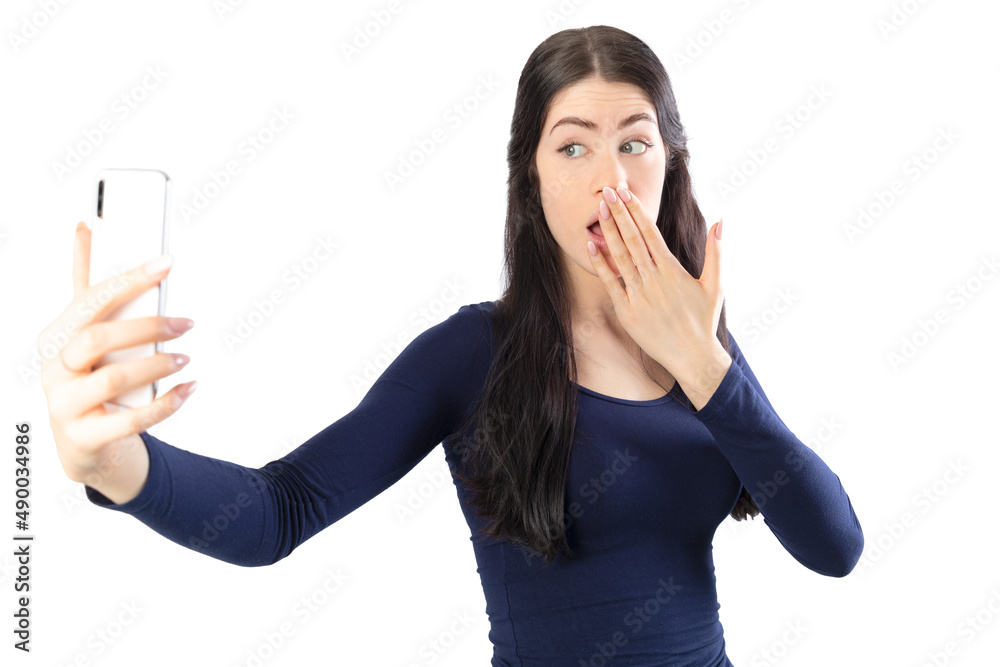 Surprised woman with his hand in the mouth taking a selfie with a smartphone. Isolated on white background. 19-20 years old caucasian woman. Surprised woman with his hand in the mouth taking a selfie with a smartphone. Isolated on white background. 19-20 years old caucasian woman.