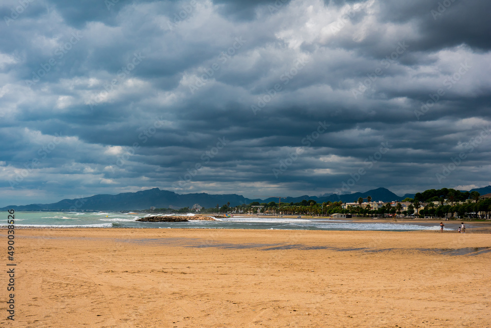 Thunderclouds over seascape with sand beach, breakwater and  mountains in background