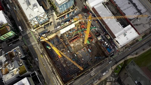 Slow moving overhead aerial of construction cranes sitting on an empty lot waiting for development.